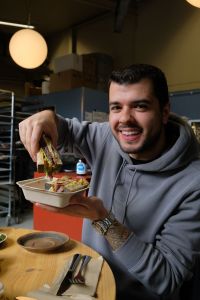 En man håller en sandwich i handen och ler in i kameran.