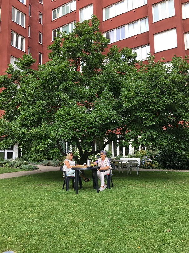 Två hyresgäster från Trygghetsboendet i Majviken sitter ute och fikar under ett träd på gården.