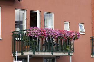 Bilden visar en balkong med blomlådor på ett hus med persikofärgad fasad