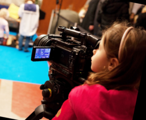 En flicka med röd tröja filmar med en stor kamera.