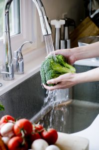 Ett par händer sköljer broccoli under rinnande vatten.